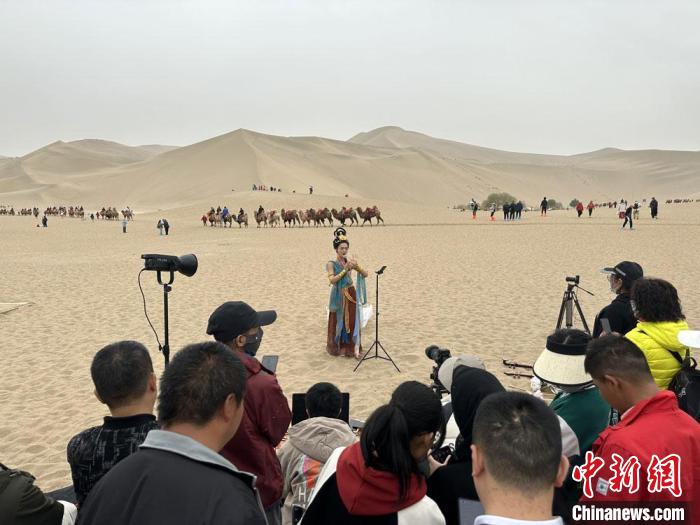 圖為2023年4月底，敦煌大漠“逐舞者”奧楠在鳴沙山月牙泉景區(qū)視頻直播，吸引游人圍觀?！●T志軍 攝