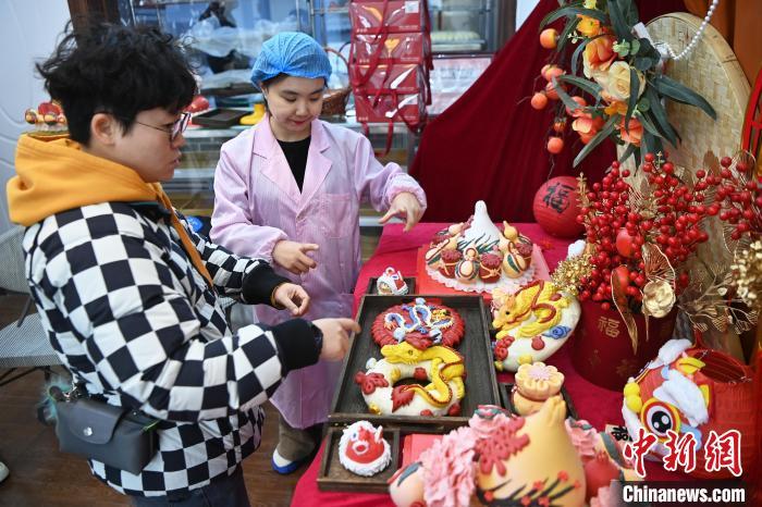 1月25日，隨著春節(jié)臨近，蘭州一花饃店“龍”元素花饃熱銷。圖為工作人員向顧客推薦“龍”元素花饃。九美旦增 攝</p><p>